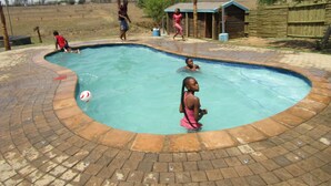 A swimming pool with a curved edge, surrounded by a brick patio. - Lily Villa Country Lodge (Emalahleni)