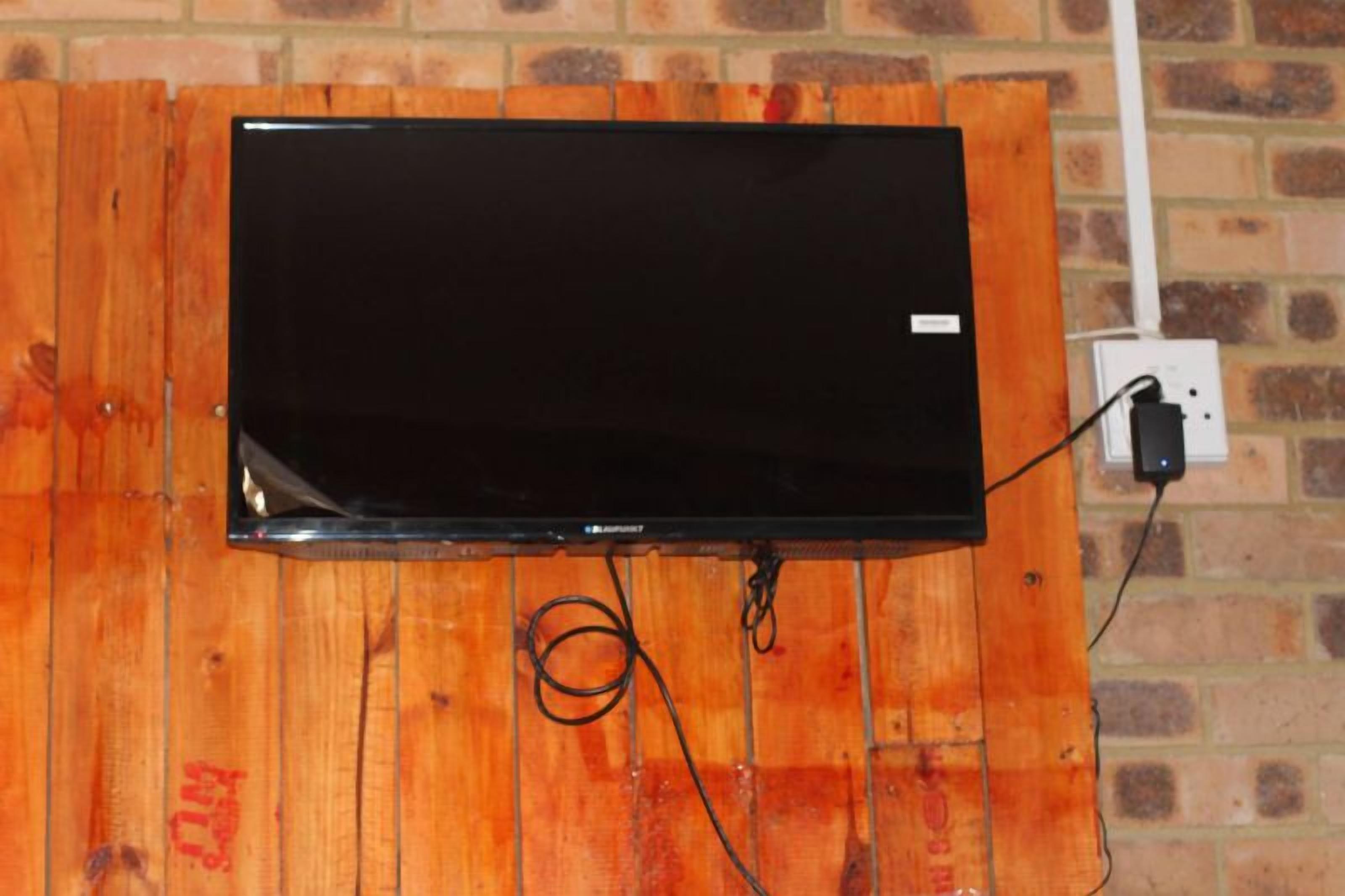 Un téléviseur à écran plat fixé sur un mur en bois, avec une prise électrique visible et un système de gestion des câbles.