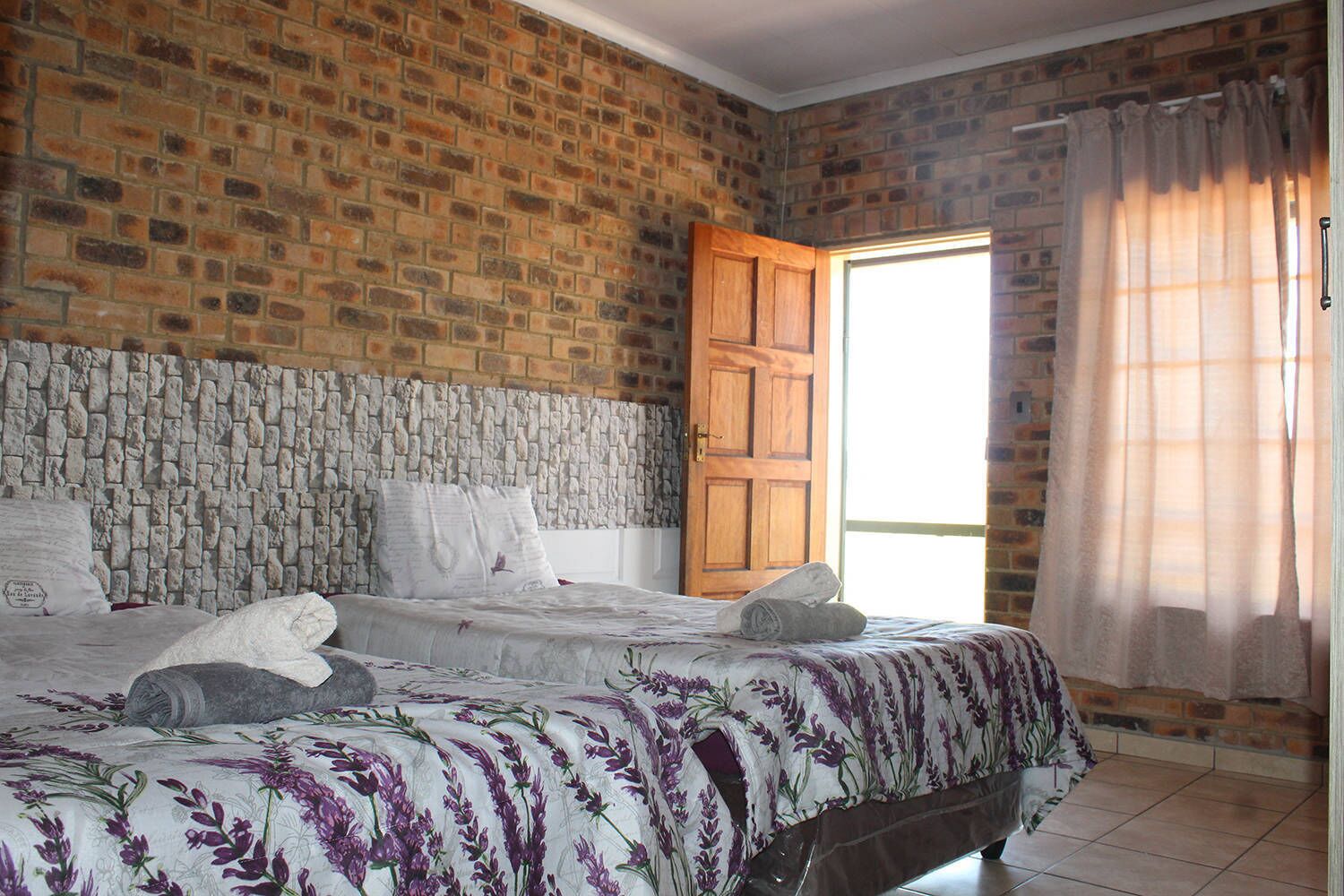 Ein Zimmer mit Backsteinwand, steinernen Kopfseitenverkleidungen, einem Bett mit floralem Bettzeug und einer Holztür.