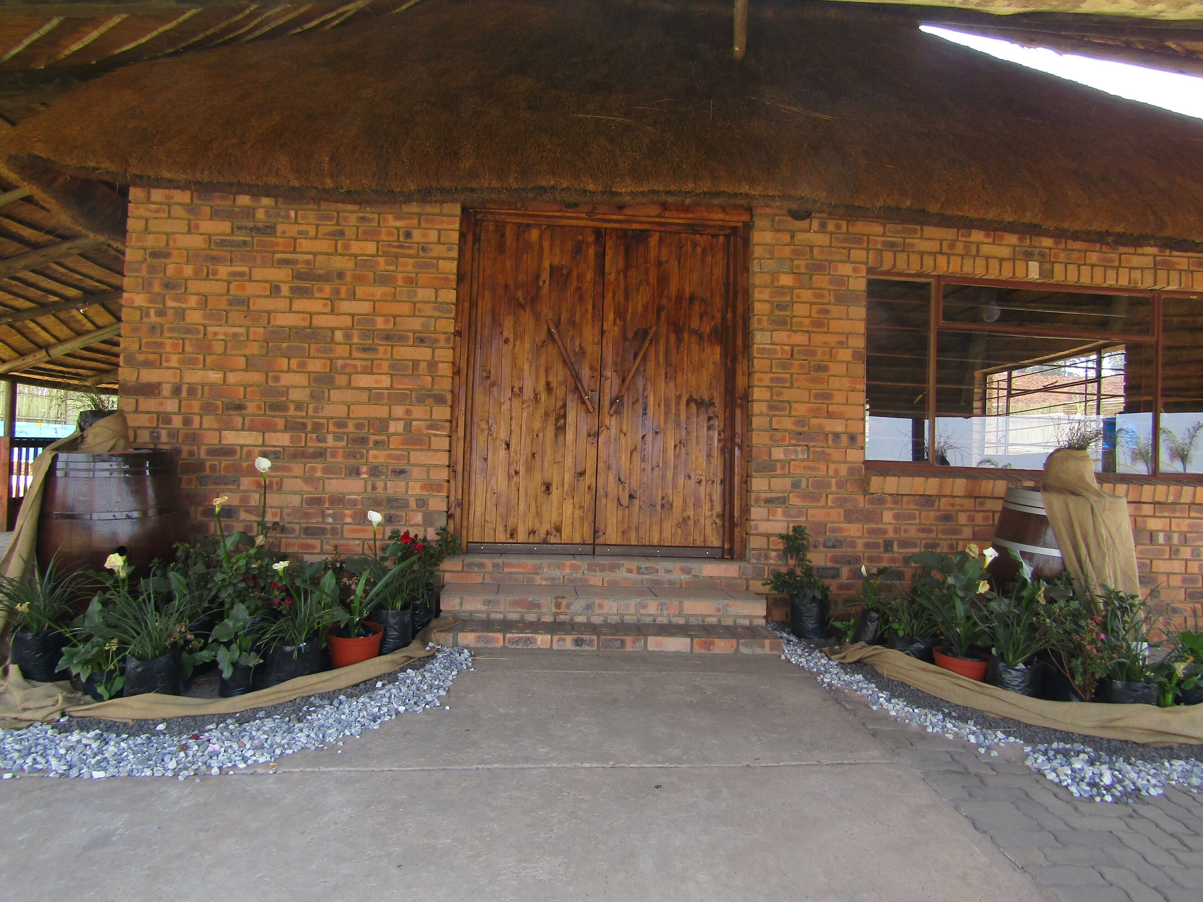 A brick building with a wooden door, potted plants, and a concrete pathway.