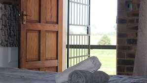 A room with a wooden door, a window with a metal grill, and a bed with a rolled-up towel. - Lily Villa Country Lodge (Emalahleni)