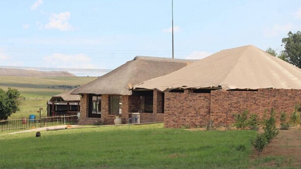 A brick building with a thatched roof and a fenced area in front. - Lily Villa Country Lodge (Emalahleni)