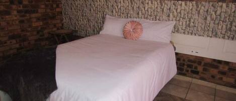 A bedroom with a brick wall, a stone headboard, a bed with a white bedspread, and a patterned rug.
