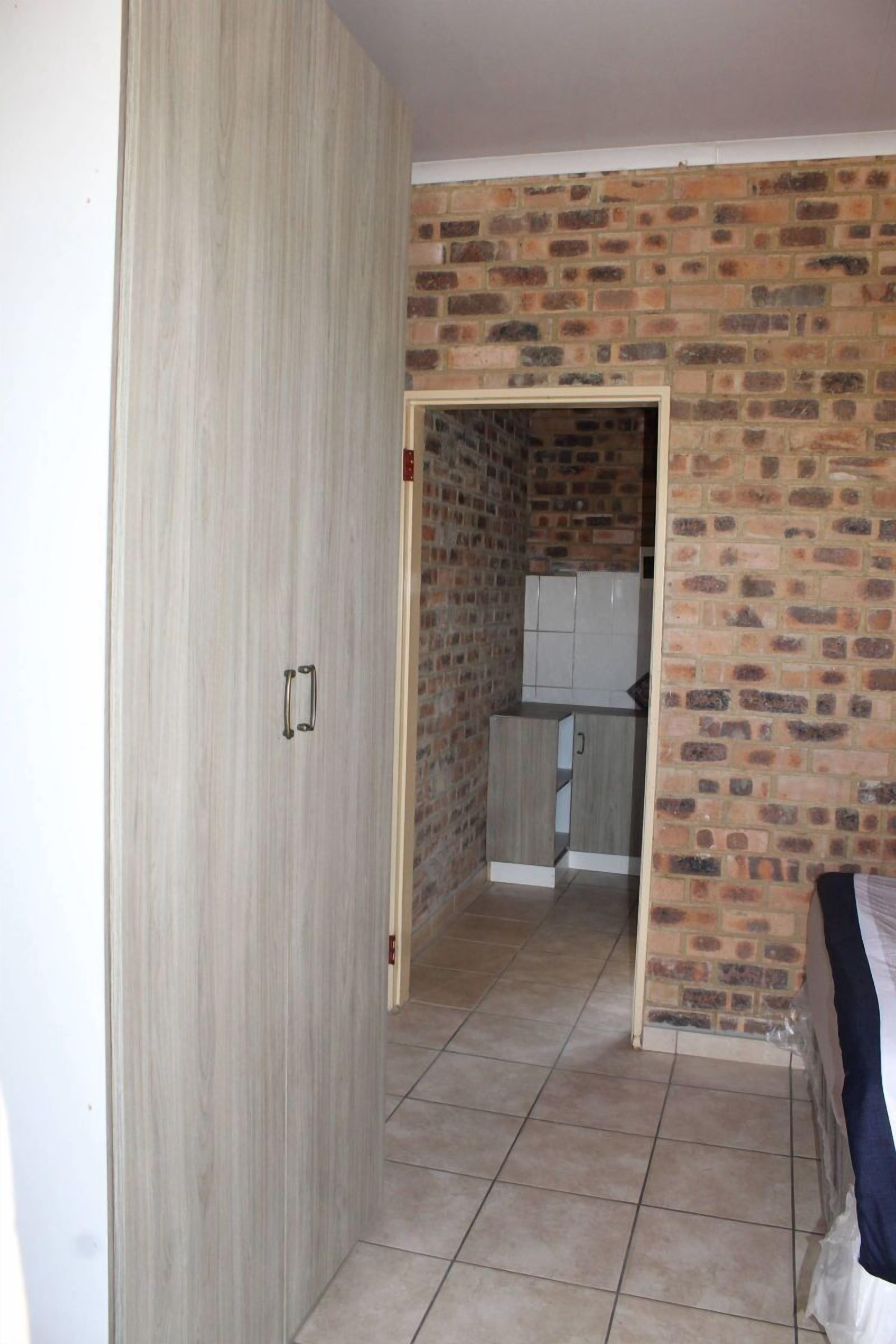 Una habitación con armario, zona de cocina con pared de ladrillo y cama.