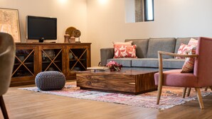 Een woonkamer met een grijze bank, een houten salontafel, een roze fauteuil en een televisie op een houten kast.