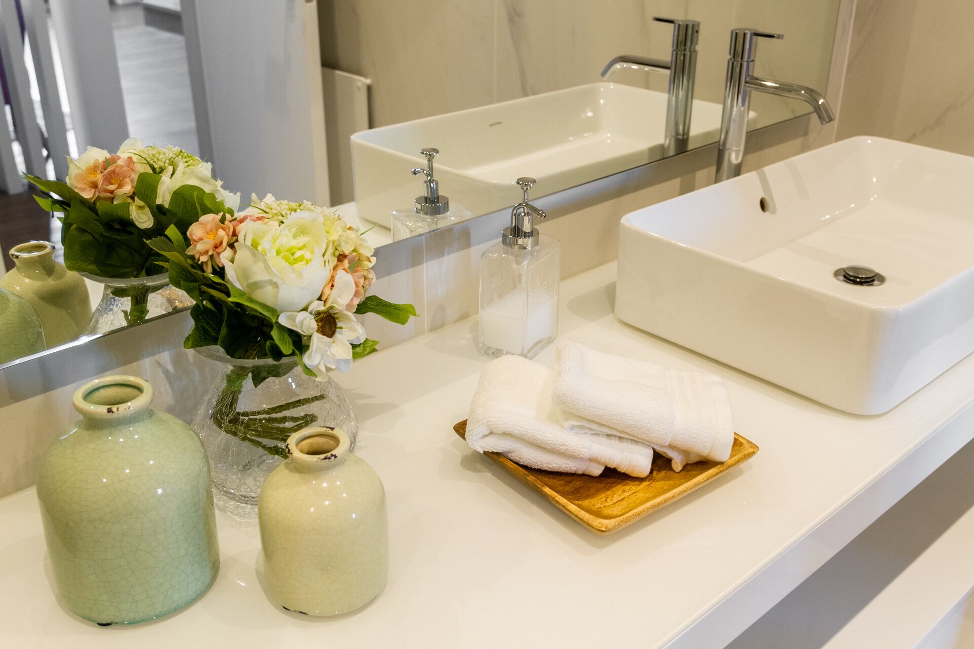 A bathroom with a white sink, a mirror, and two vases with flowers.