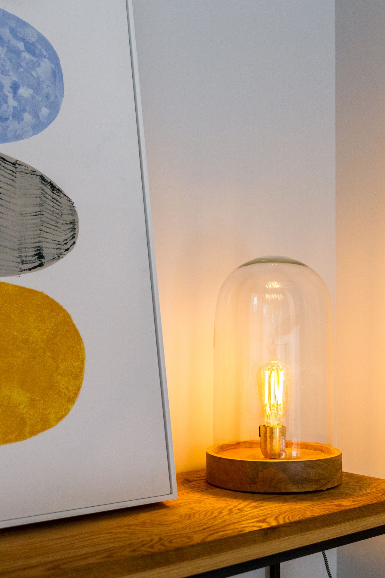A table with a framed abstract painting and a glass dome light fixture.