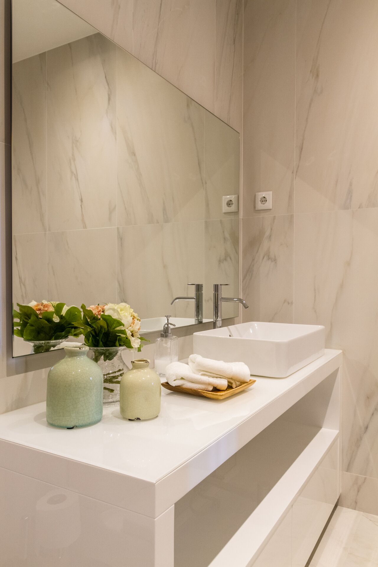Ein modernes Badezimmer mit großem Spiegel, weißem Waschbecken und Marmorrückwand.