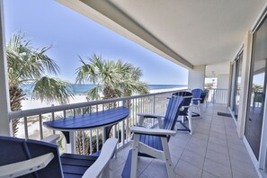 En balkon med udsigt over stranden, med blå stole og et bord.