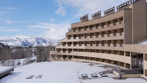 Un edificio de varios pisos con fachada curva, balcones y un paisaje nevado con montañas al fondo.