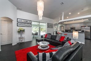 A modern living room with a black leather sofa, a red rug, and a glass coffee table. There are two pendant lights, a fireplace, and a kitchen in the background. - Stunning Executive Ruyper 4 Bedroom Home by RedAwning (Inverness)