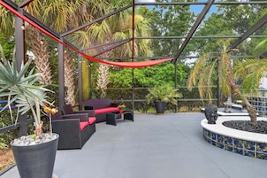 An outdoor patio with wicker furniture, a red canopy, and tropical plants.