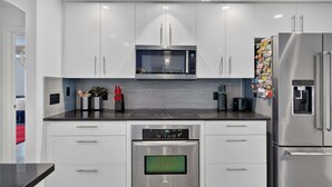 A modern kitchen with white cabinets, a stainless steel microwave, oven, and refrigerator. - Stunning Executive Ruyper 4 Bedroom Home by RedAwning (Inverness)