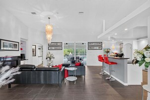 Un interior moderno con un sofá de cuero negro, una zona de comedor con taburetes de bar rojos y una cocina con encimera blanca.