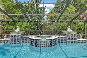Zona de piscina con jacuzzi, rodeada por una estructura de metal y paneles de vidrio, y estatuas en el borde del jacuzzi.