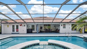 A swimming pool with a tiled edge, a covered patio area with a table and chairs, and a building with a tiled roof. - Stunning Executive Ruyper 4 Bedroom Home by RedAwning (Inverness)