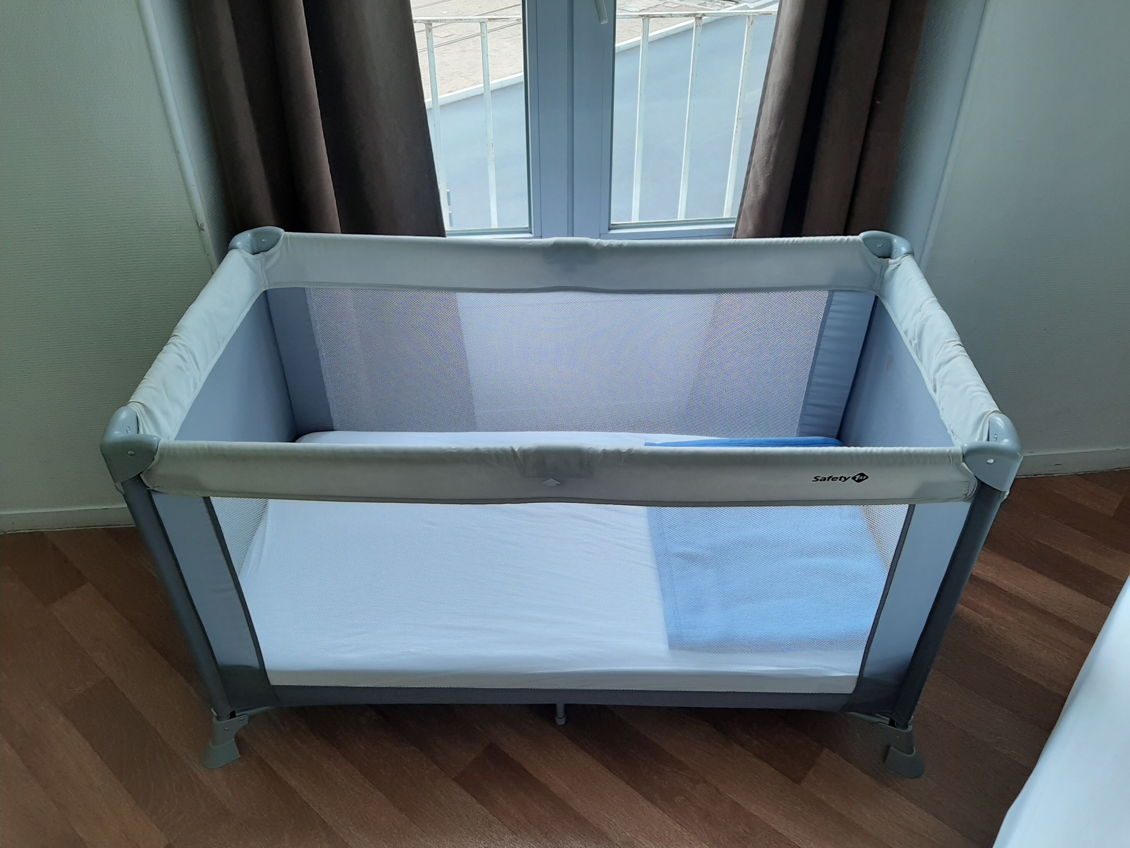 Una cuna para bebé con barandilla de seguridad, ubicada cerca de una ventana con cortinas.