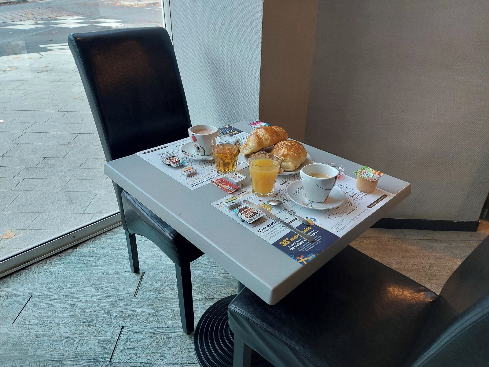 Una mesa de desayuno con croissants, una taza de café, un vaso de jugo de naranja y un periódico.