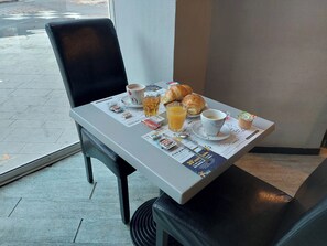 A breakfast table with croissants, a cup of coffee, a glass of orange juice, and a newspaper. - Hotel Le Royalty (Angers)