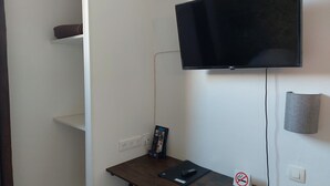 A small room with a flat-screen TV mounted on the wall, a desk with a laptop, a remote control, and a "no smoking" sign. - Hotel Le Royalty (Angers)