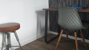 A corner of a room with a wooden floor, a metal-framed stool, a chair with a quilted backrest, and a wooden desk against a wall with a leaf-patterned curtain. - Hotel Le Royalty (Angers)