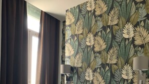A hotel room with a large bed, dark curtains, a floral wallpaper, and two wall-mounted lamps. - Hotel Le Royalty (Angers)