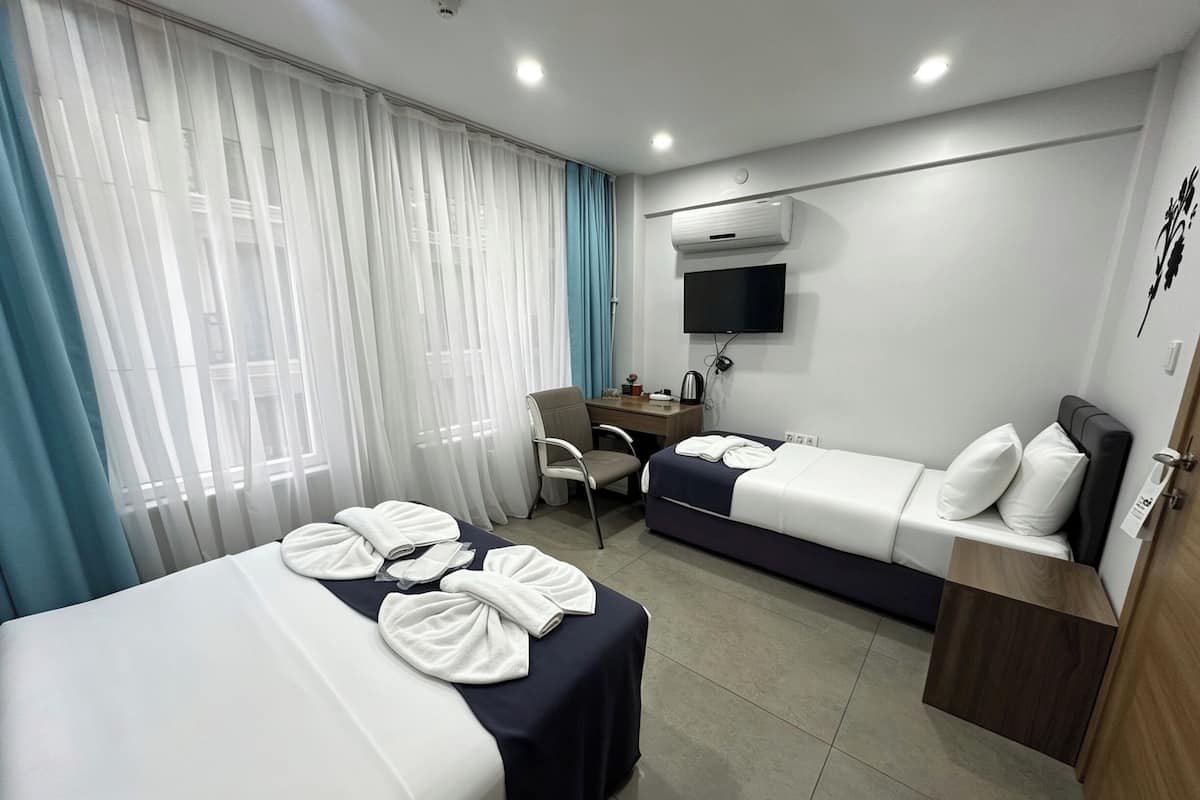 A hotel room with two beds, a desk, a chair, a TV, and an air conditioning unit.