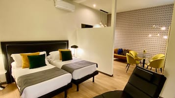 A hotel room with two beds, a modern chandelier, an air conditioning unit, a patterned wall, and a seating area with yellow chairs.