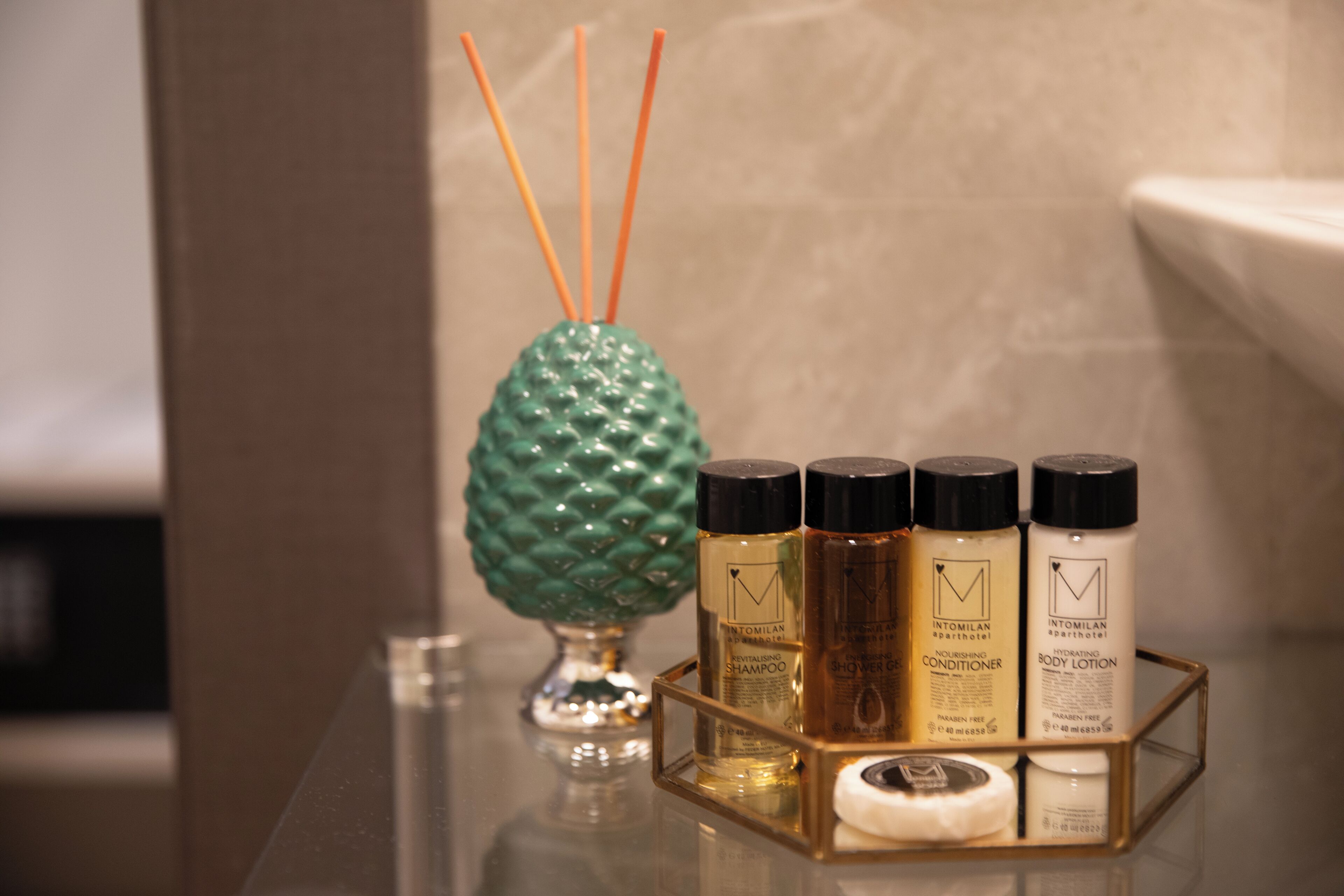 Un lavabo da bagno con un contenitore in vetro pieno di articoli da toilette, un vaso decorativo a forma di ananas e un vassoio con quattro flaconi di prodotti per la cura del corpo Intomilan.