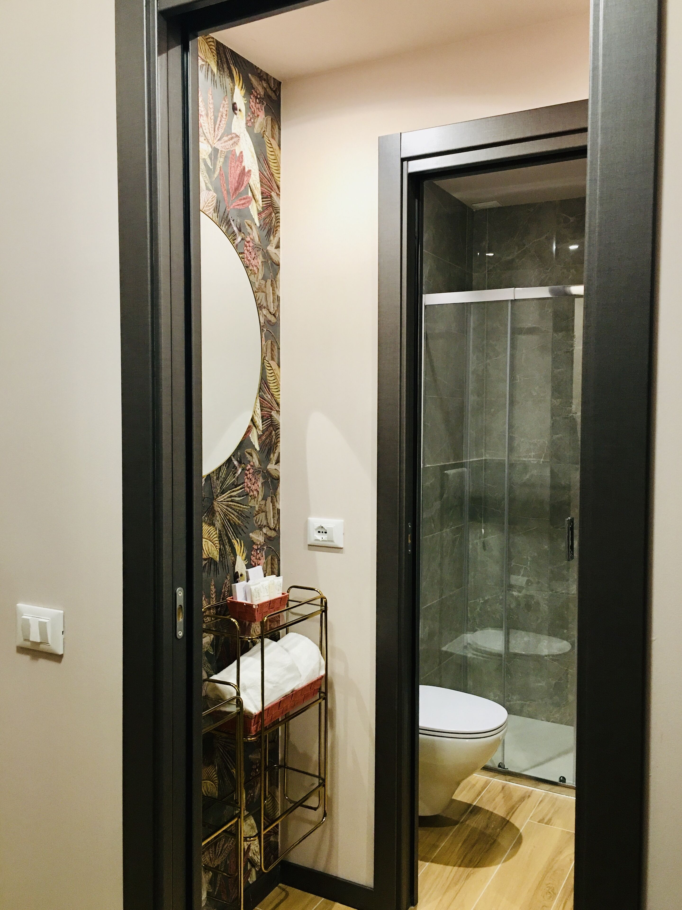 A bathroom with a shower, a toilet, a sink with a towel, and a decorative wall.