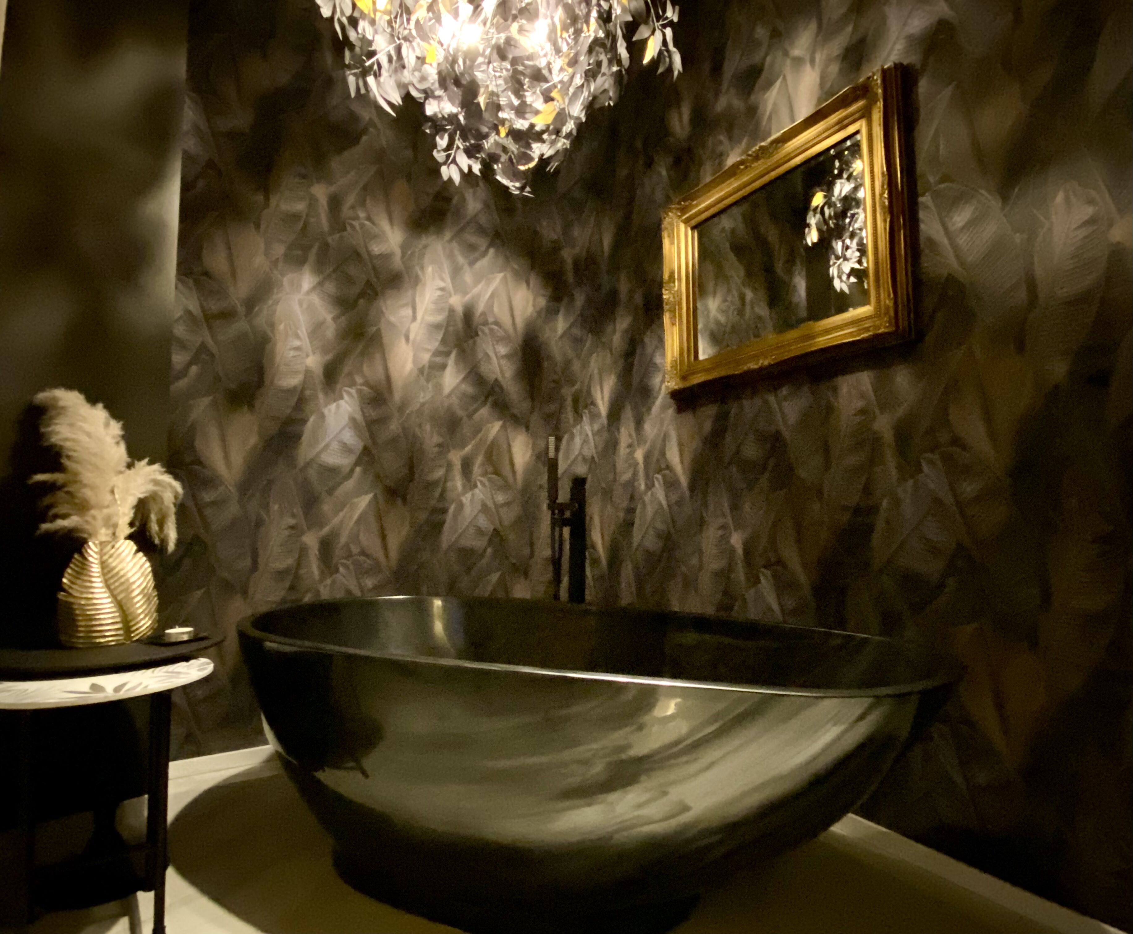 A large, modern sink with a reflective surface, a small table with a decorative vase, and a framed mirror on the wall.