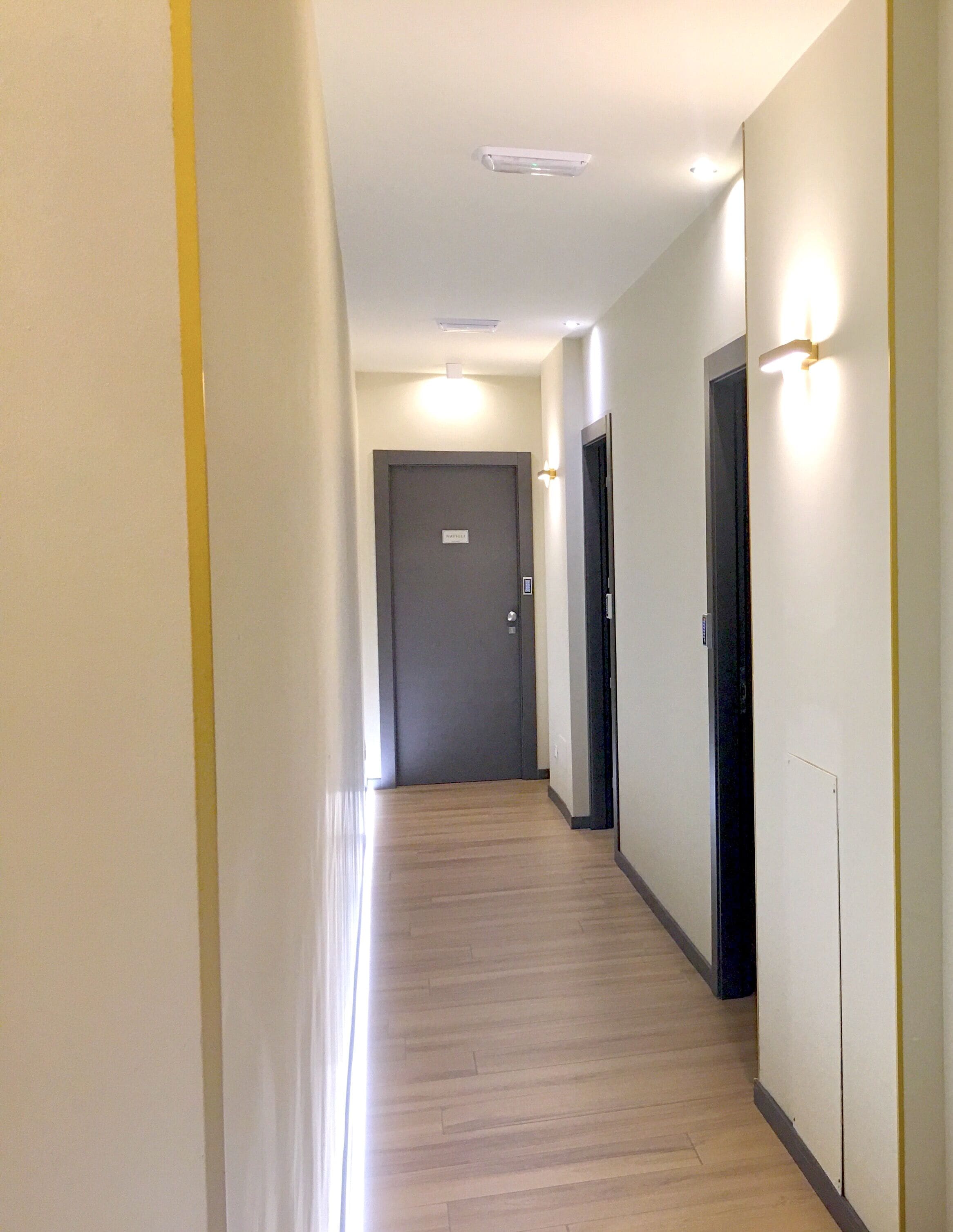Un couloir doté d’un plancher en bois, de murs blancs et de portes à cadre noir.