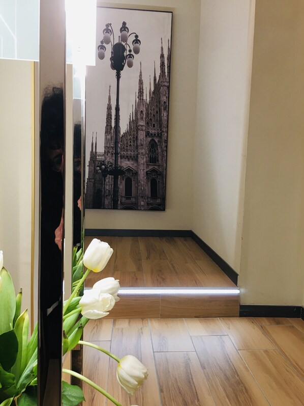 A hallway with a wooden floor, a large framed picture of a Gothic cathedral, and a white flower arrangement. - INTOMILAN  Galleria Duomo - Boutique & Design Aparthotel (Milan)
