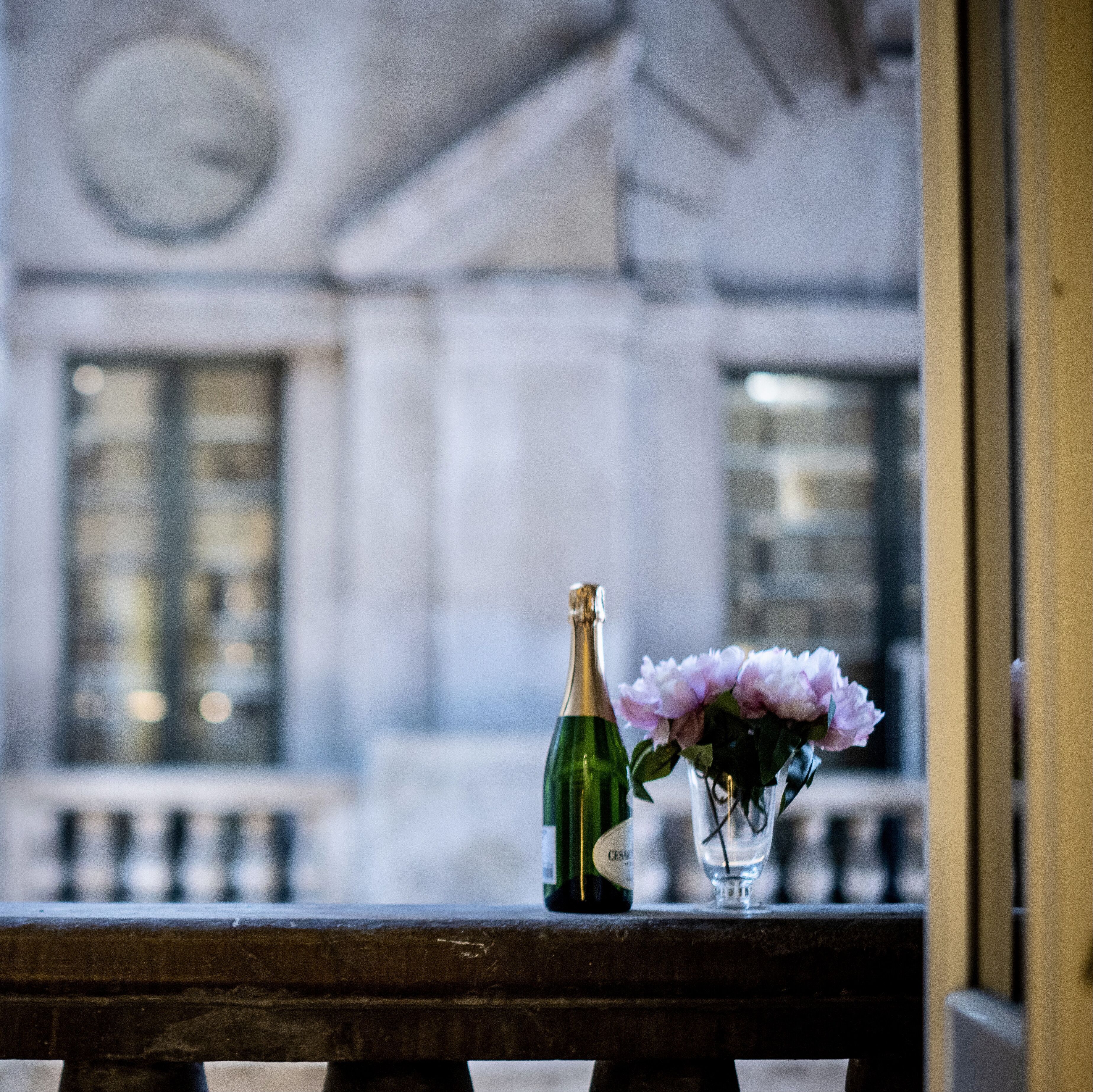 Une bouteille de champagne et un vase rempli de fleurs, posés sur le rebord d’une fenêtre.