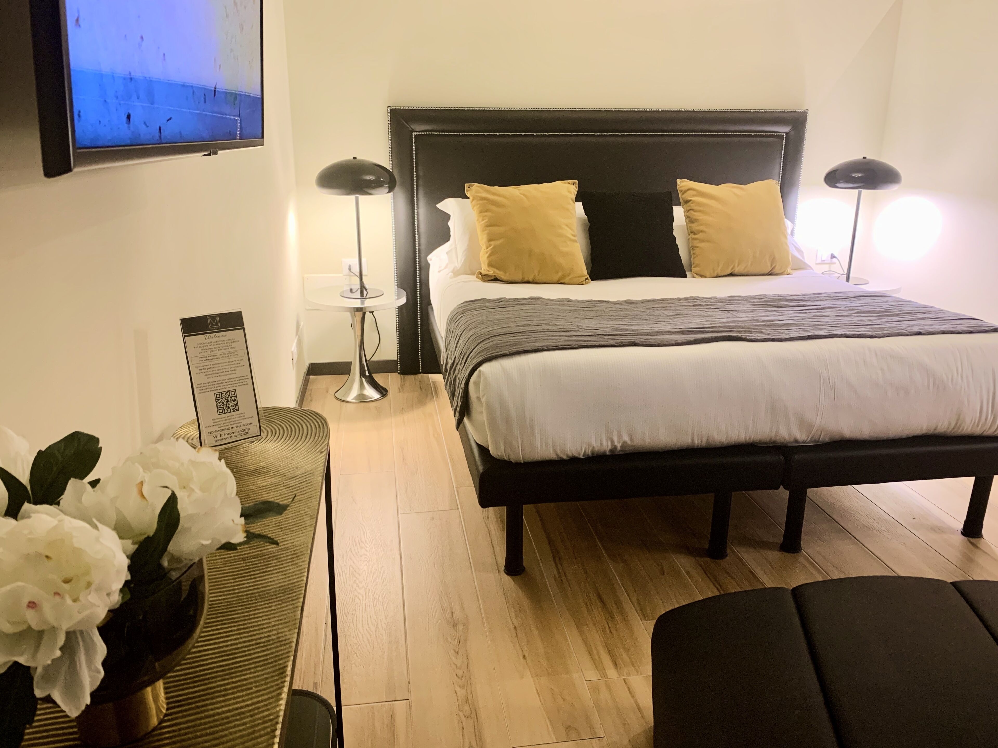 Ein ordentlich eingerichtetes Hotelzimmer mit Bett, Nachttischlampen, einem kleinen Tisch und einer Blumenvase.