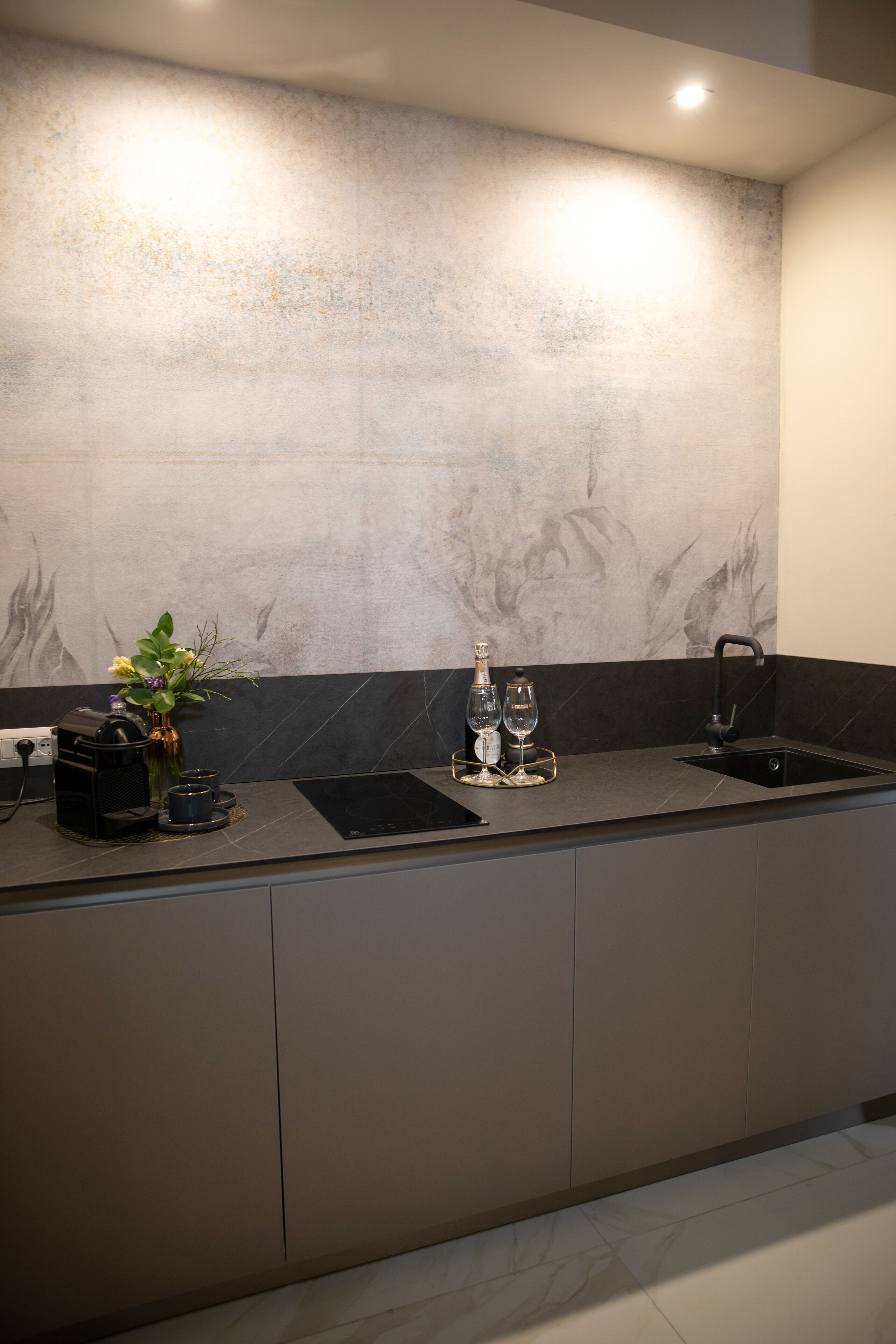 A modern kitchen with a marble backsplash, a built-in sink, and a countertop with a coffee machine and a vase with flowers.