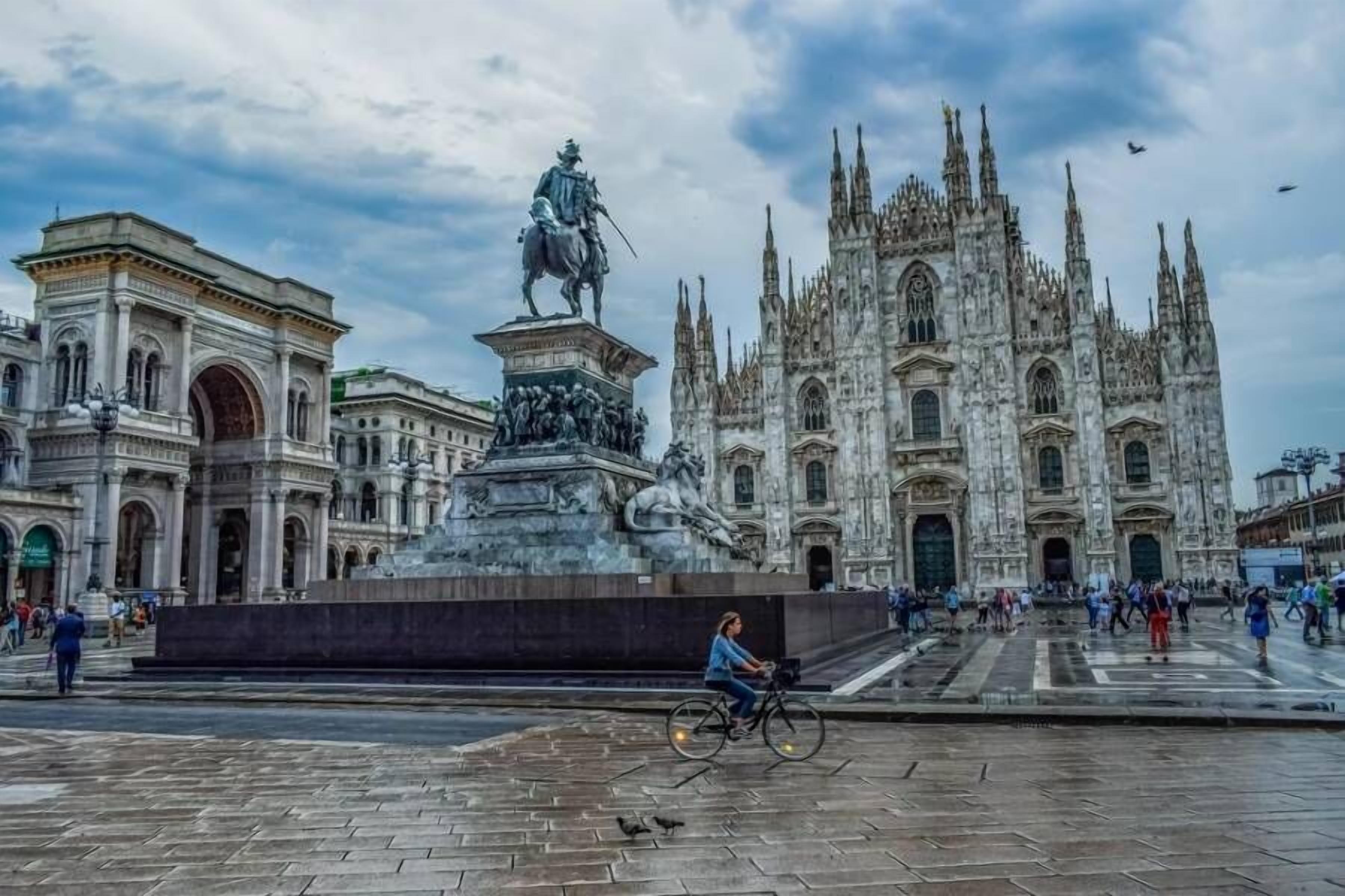 A plaza with a statue, a cathedral, and a building with arched windows.