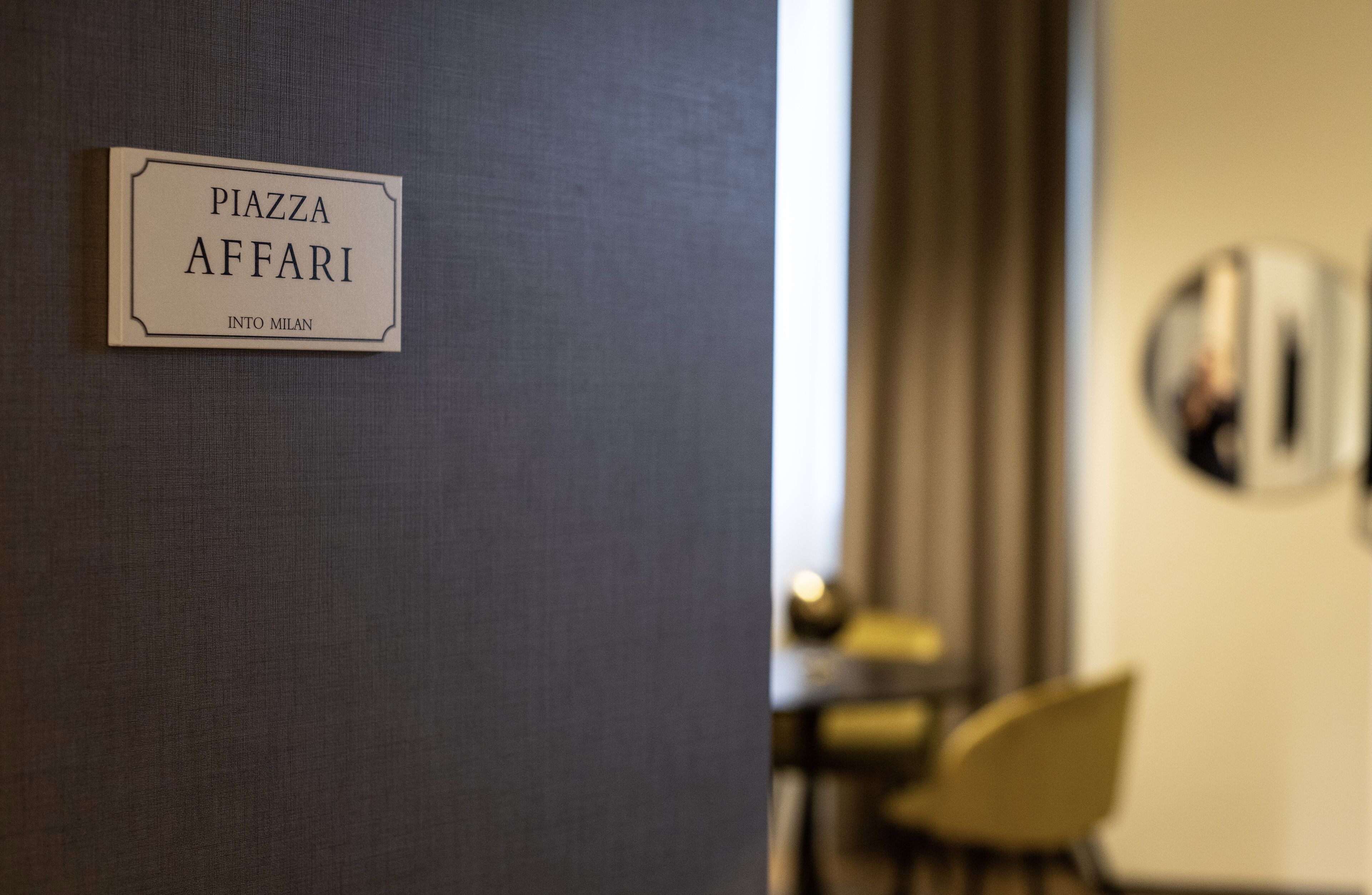 Una señal que dice "PIAZZA AFFARI INTO MILAN" en una pared.
