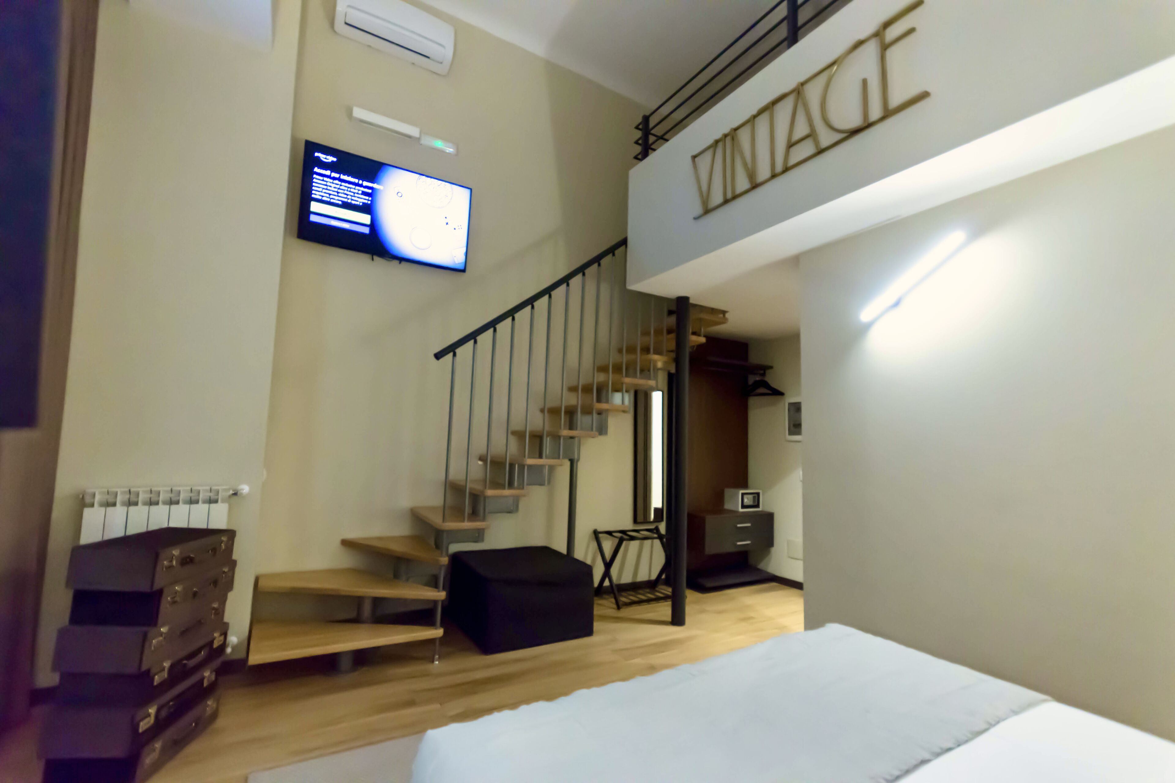 A bedroom with a bed, a TV mounted on the wall, a staircase, and a wardrobe.