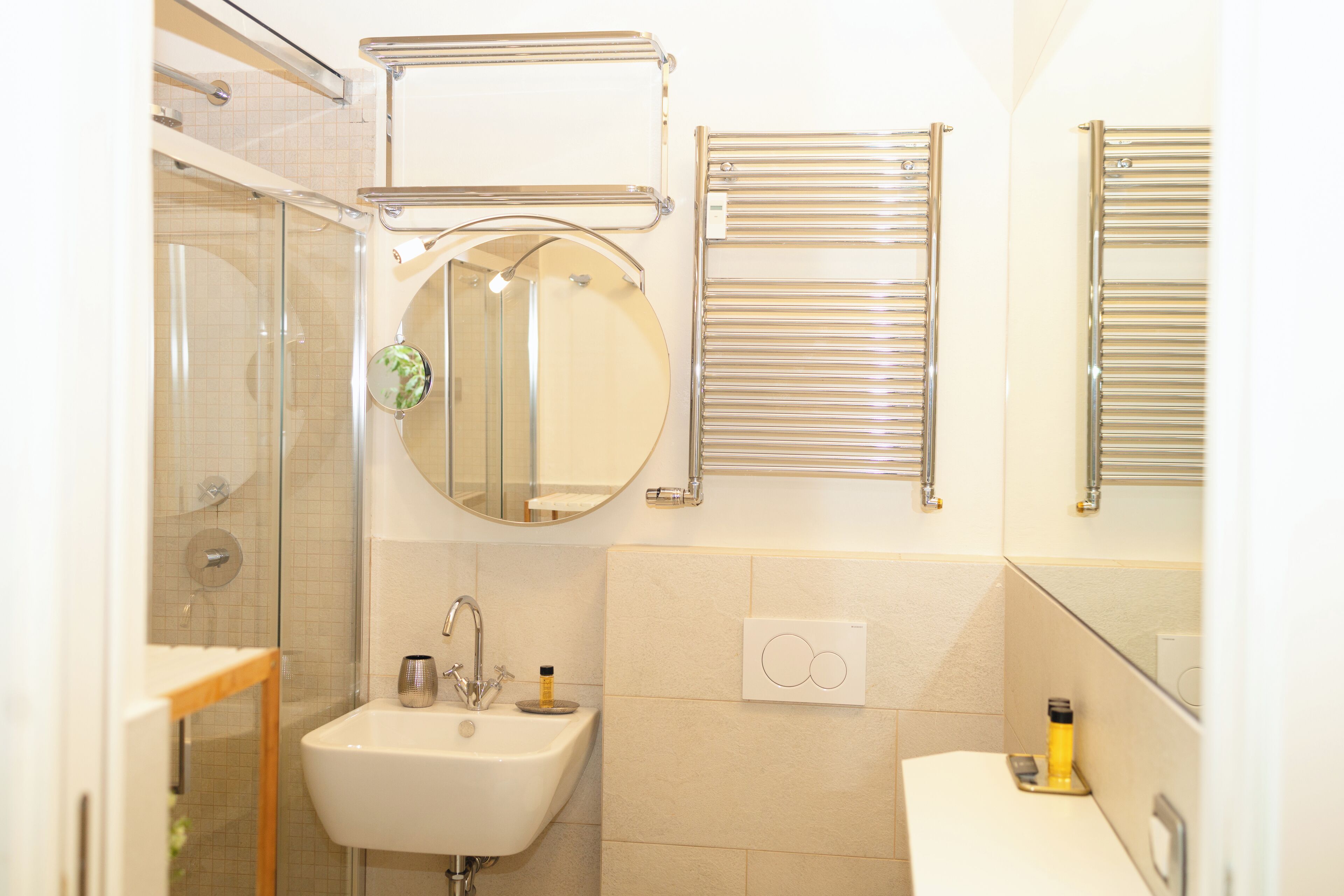 A bathroom with a glass shower enclosure, a sink with a mirror above it, and towel racks on the wall.