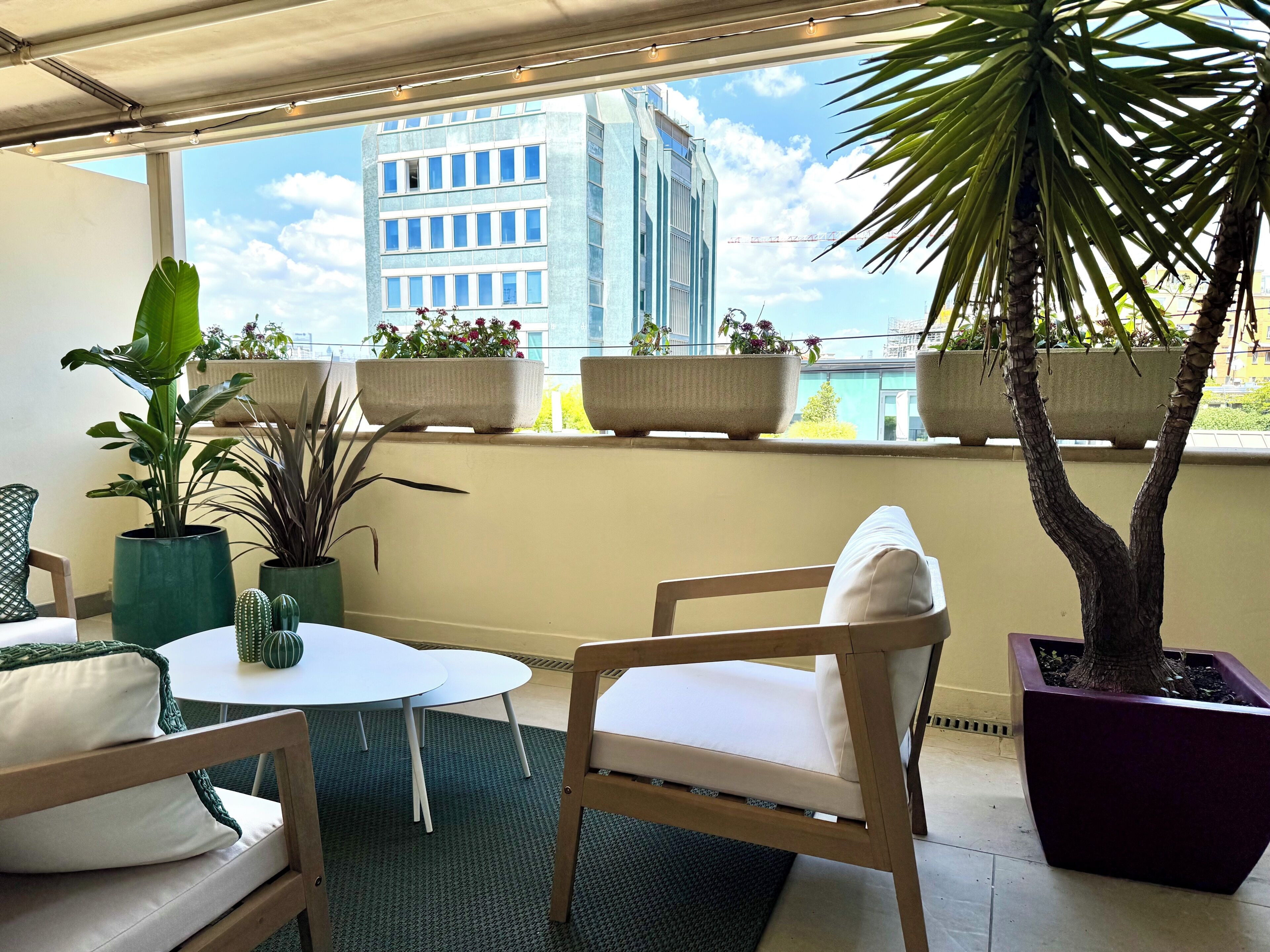 Ein Balkon mit Blick auf ein Gebäude, mit Blumentöpfen, einem weißen Tisch und einem Holzstuhl.