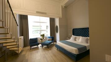 Ein Hotelzimmer mit Bett, einer Couch, einem kleinen Tisch mit einer Vase, einer Treppe und einem Fenster mit Vorhängen.