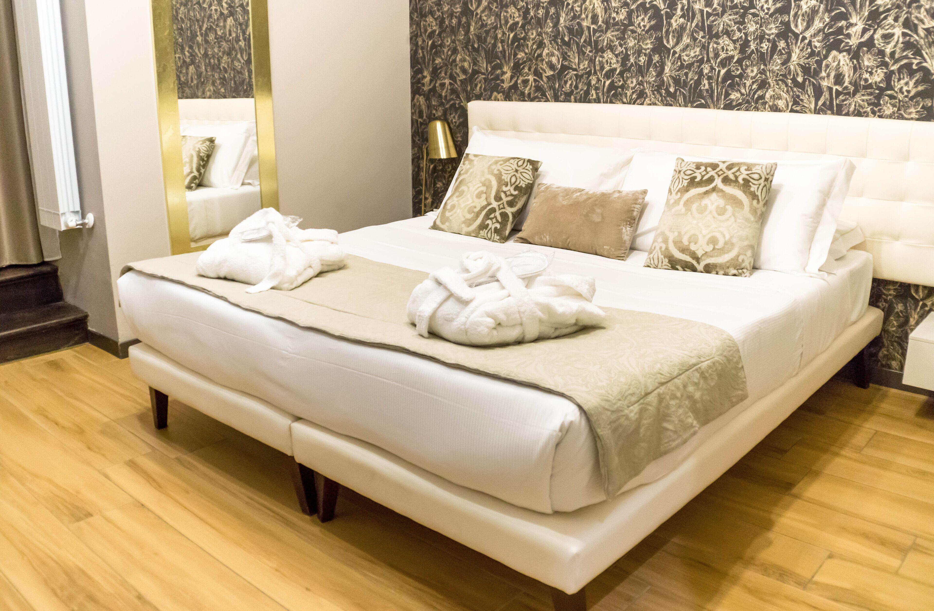 A hotel room with a large bed, a bedside table, a mirror, and a patterned wallpaper.
