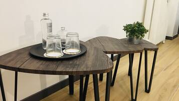 A room with two wooden tables, one with a tray holding three glass containers and a bottle, and another with a potted plant.