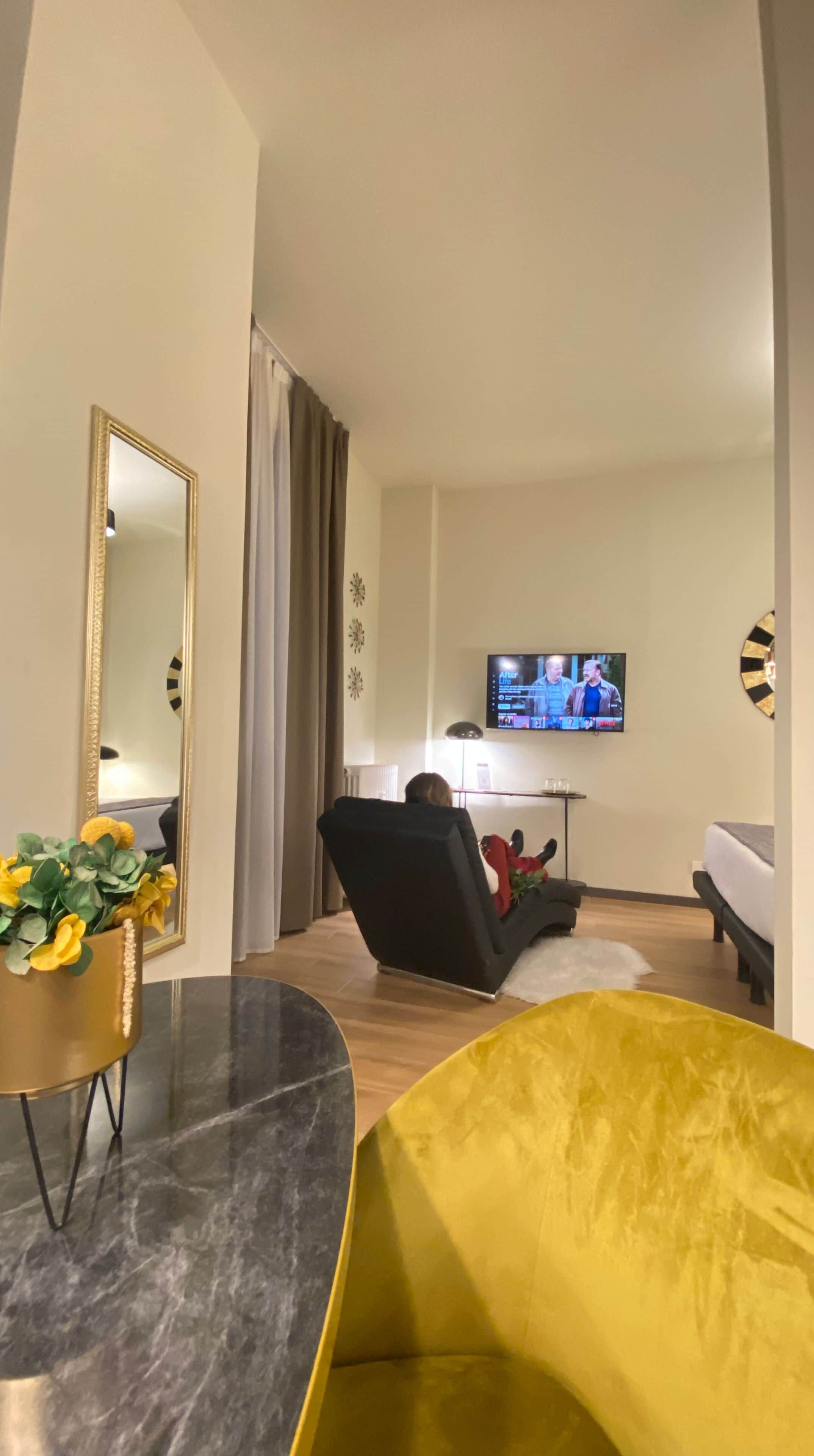 Una sala de estar moderna con un televisor de pantalla plana montado en la pared, un sofá de cuero negro, un sillón amarillo y una mesa de centro redonda.