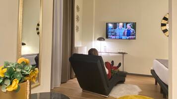 Una sala de estar moderna con un televisor de pantalla plana montado en la pared, un sofá de cuero negro, un sillón amarillo y una mesa de centro redonda.