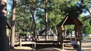 Un parque infantil con tobogán, columpios y un pequeño refugio de madera.