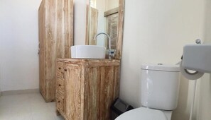 A bathroom with a wooden vanity, a white sink, and a toilet. - Laksmi Guest House (Canggu)