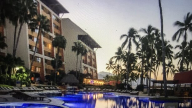 A hotel pool with palm trees and a building in the background. - Ocean view 1King Bedroom/2BA, kitchen, private balcony, sofa bed, beachfront (Puerto Vallarta)