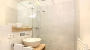 A modern bathroom with a glass-enclosed shower, a wooden vanity with a sink, and a towel rack. - Hubertushöhe (Regensburg)